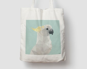 May include: A white tote bag featuring a geometric, low-poly illustration of a cockatoo. The bird is rendered in shades of white and gray with a yellow crest, set against a light blue square background. The design has a clean, angular aesthetic.
