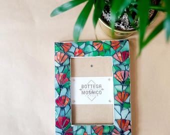 May include: A mosaic picture frame with a green and red floral design. The frame is made of small pieces of glass and has a rectangular shape. The frame is empty and ready to hold a picture. The text "Bottega del Mosaico Artigiana" is visible on the frame.