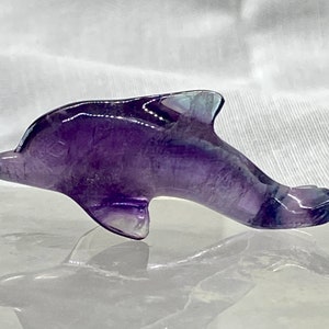 May include: A purple and blue fluorite dolphin figurine. The dolphin is carved from a single piece of fluorite and has a smooth, polished finish.