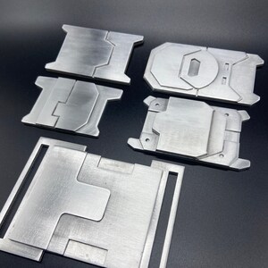K&ouml;nnte beinhalten: F&uuml;nf Metallplatten in verschiedenen Formen und Gr&ouml;&szlig;en. Die Platten sind aus geb&uuml;rstetem Metall und haben eine silberne Oberfl&auml;che.