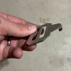 May include: A silver metal hook with a rectangular loop. The hook is designed to be attached to a belt or bag.