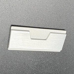 Op de afbeelding: Een rechthoekig, lichtgrijs object met een verzonken middengedeelte. Het object heeft een textuuroppervlak en lijkt van metaal of een vergelijkbaar materiaal te zijn gemaakt. Het is geplaatst tegen een donkergrijze achtergrond.