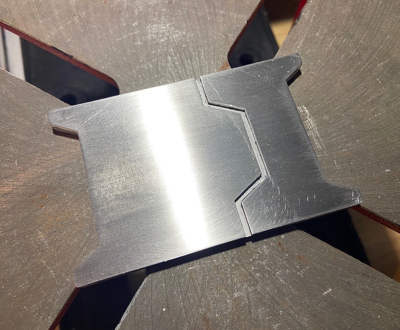 May include: A close-up of a silver metal piece with a smooth, brushed finish. The piece has a unique shape with two cutouts on one side. The piece is likely a part of a larger metal object.