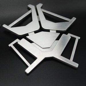 May include: A silver metal stand with a geometric design. The stand has three legs and a flat top.