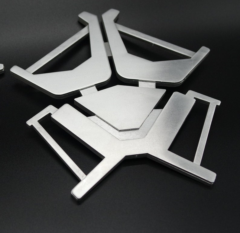 May include: A silver metal stand with a geometric design. The stand has three legs and a flat top.