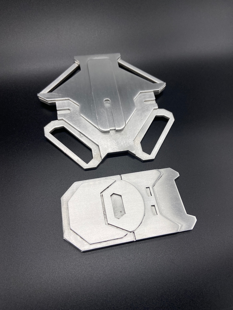 May include: Two silver metal pieces, one shaped like a star with a hole in the centre, and the other a rectangular shape with a rounded edge and a hole in the centre.