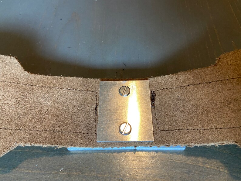 May include: A close-up of a metal plate with two screws attached to a piece of brown leather.