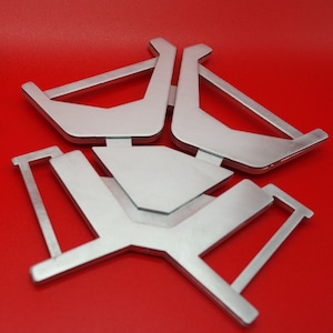 May include: Silver metal stand with three legs and a rectangular top. The stand is designed to hold a small object, such as a phone or a tablet.