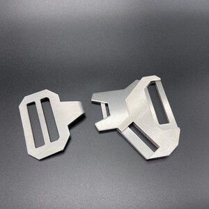 May include: Two silver metal belt buckle closures. One is a standard buckle with two slots, the other is a more complex design with a single slot.