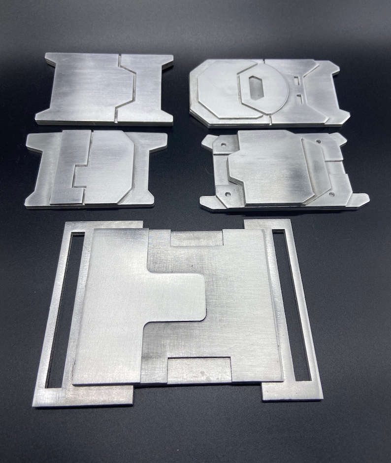 K&ouml;nnte beinhalten: F&uuml;nf Metallteile, m&ouml;glicherweise f&uuml;r ein DIY-Projekt, sind auf einer schwarzen Oberfl&auml;che angeordnet. Die Teile sind silberfarben und haben eine geb&uuml;rstete Oberfl&auml;che. Das gr&ouml;&szlig;te Teil ist rechteckig mit einem Ausschnitt in der Mitte. Die anderen Teile sind kleiner und haben verschiedene Formen.
