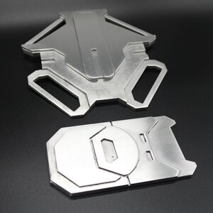 May include: Two metal pieces, one with a geometric shape and the other with a rounded shape, both with a brushed silver finish.