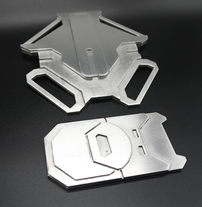 May include: Two metal pieces, one with a geometric shape and the other with a rounded shape, both with a brushed silver finish.