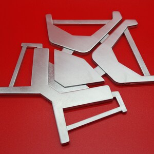 May include: Three silver metal pieces with geometric shapes, forming a star-like pattern against a red background.