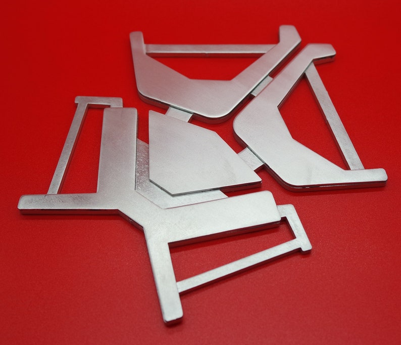 May include: Three silver metal pieces with geometric shapes, forming a star-like pattern against a red background.