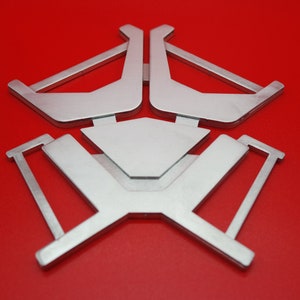 May include: A silver metal stand with a geometric design. The stand has a triangular shape with three arms that extend outward. The stand is on a red background.
