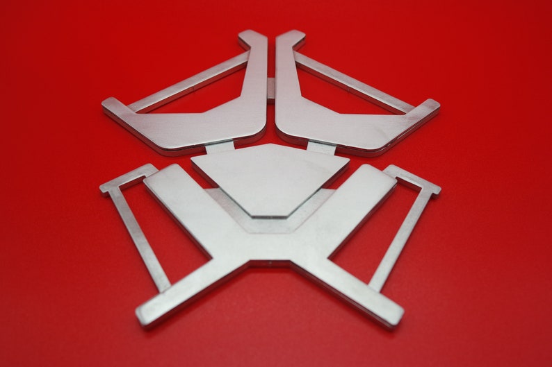 May include: A silver metal stand with a geometric design. The stand has a triangular shape with three arms that extend outward. The stand is on a red background.