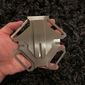 May include: A silver metal keychain with a geometric design. The keychain has a smooth, brushed finish and a key ring attached.