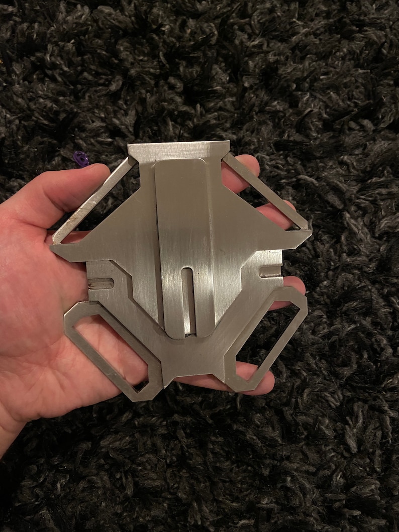 May include: A silver metal keychain with a geometric design. The keychain has a smooth, brushed finish and a key ring attached.
