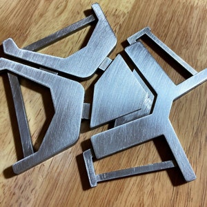 May include: A silver metal trivet with a geometric design. The trivet is made of three interlocking pieces that form a star shape.