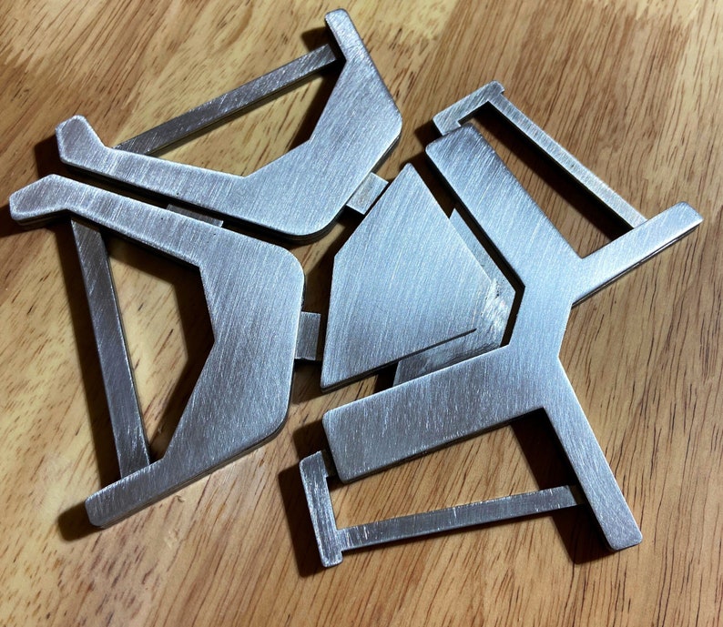 May include: A silver metal trivet with a geometric design. The trivet is made of three interlocking pieces that form a star shape.