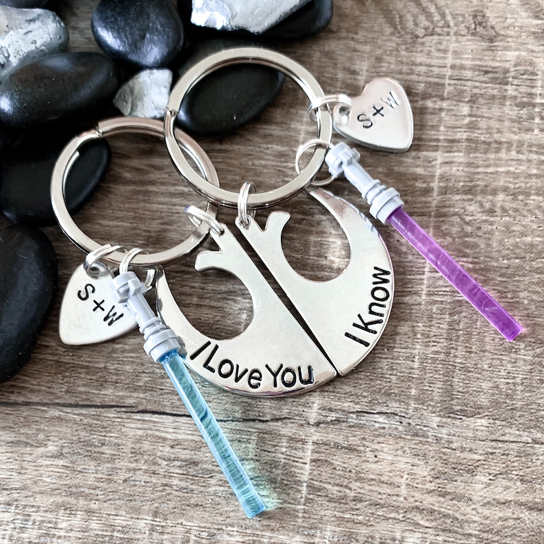 Puede incluir: Un juego de dos llaveros plateados con tem&aacute;tica de Star Wars. Los llaveros tienen forma de Halc&oacute;n Milenario y llevan el texto "I Love You" y "I Know". Los llaveros tambi&eacute;n incluyen dos peque&ntilde;os sables de luz, uno azul y otro morado, y un dije en forma de coraz&oacute;n con las iniciales "S+W".