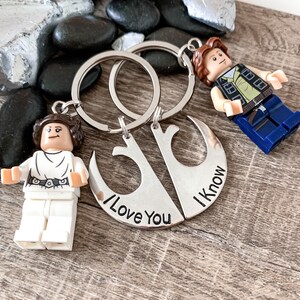 Pu&ograve; includere: Un portachiavi d'argento con due forme di mezzaluna intrecciate. Il portachiavi presenta il testo "I Love You" e "I Know" su ogni lato. Il portachiavi &egrave; attaccato a due anelli con una minifigure Lego Star Wars di Principessa Leia e Han Solo.