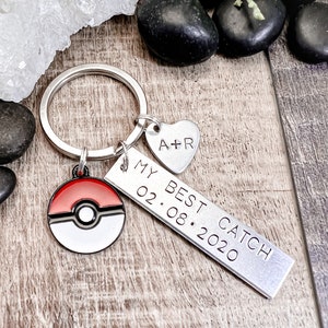 May include: Silver keychain with a red and white Pokeball charm, a silver heart charm with the initials "A+R" engraved, and a silver bar charm with the text "My Best Catch 02.08.2020"