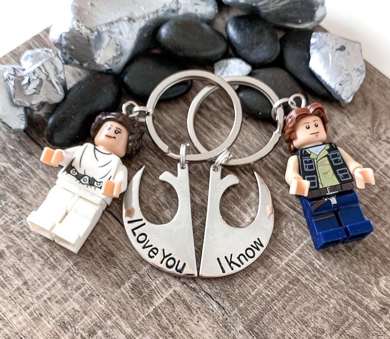 Pu&ograve; includere: Un portachiavi argentato con due simboli dell'Alleanza Ribelle che si intrecciano. I simboli sono incisi con il testo "I Love You" e "I Know". Il portachiavi presenta una minifigure Lego di Principessa Leia e Han Solo.