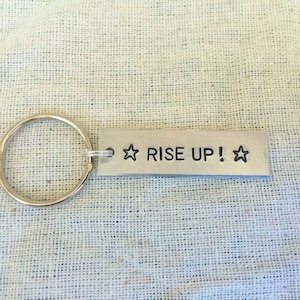 May include: Silver keychain with a rectangular tag that reads "RISE UP!" with a star on each side.