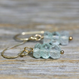 Puede incluir: Un par de pendientes de oro con cuentas de piedras preciosas de color azul claro. Los pendientes tienen un diseño simple y minimalista.