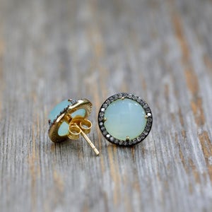 Op de afbeelding: Een paar gouden oorbellen met een lichtblauwe edelsteen omringd door een halo van kleine diamanten.