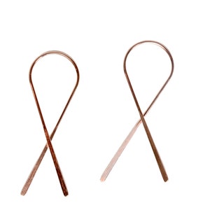 Può includere: Un paio di orecchini in oro rosa con un design semplice e minimalista. Gli orecchini hanno la forma di un otto, con i due anelli che si incrociano al centro.
