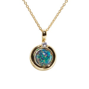 May include: A gold chain necklace with a round pendant featuring a blue-green opal surrounded by a gold bezel and a small clear gemstone.