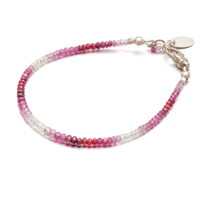 May include: A delicate bracelet made with a gradient of pink, red, and white gemstones. The bracelet is made with small, round beads and has a silver clasp.