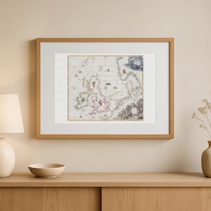 Op de afbeelding: Een ingelijste antieke kaart van de Britse eilanden, met gedetailleerde cartografie en historische elementen. De kaart is gevat in een lichtbruine houten lijst met een witte passe-partout, voor interieurdecoratie.