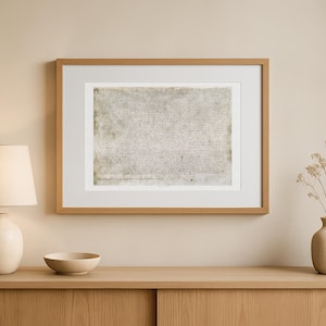 May include: A framed historical document with handwritten text. The document is centered within a white mount and a light brown wooden frame. The frame is displayed on a light brown wooden cabinet, with a lamp and a bowl.