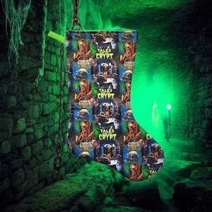 May include: A Christmas stocking with a repeating pattern featuring a red-haired ghoul and the text "TALES FROM THE CRYPT" on a black background. The stocking is hanging from a chain in a green-lit, stone-walled setting.