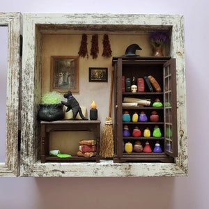 May include: A miniature witch's workshop diorama with a black cat, a cauldron, a broom, and a bookshelf filled with potion bottles and books. The diorama is framed in white wood with a distressed finish.
