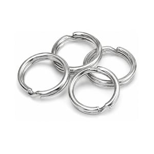 May include: A collection of four circular silver-toned metal split rings arranged in a cluster. Each ring features a double-loop coil design with a smooth, reflective finish, commonly used for attaching keys or small items to a keychain or hardware.