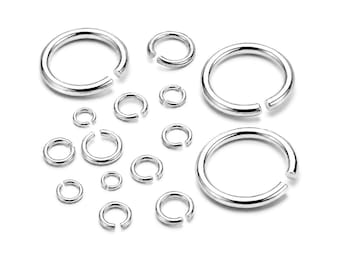 May include: A collection of silver-colored metal jump rings in various sizes, each featuring a single open gap. These circular connectors are polished with a smooth, reflective finish and are arranged in a scattered pattern on a plain surface.