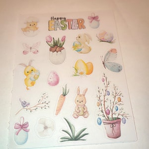 Op de afbeelding: Een vel met kleurrijke Pasen stickers met konijnen, kuikens, eieren, bloemen en een wortel. De stickers zeggen "Happy Easter" bovenaan.