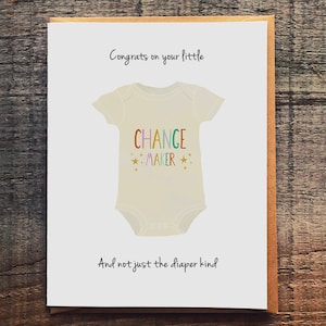 May include: A white card with a baby onesie on it. The onesie has the words "Change Maker" written on it in rainbow colors. The card says "Congrats on your little Change Maker. And not just the diaper kind."