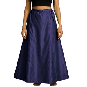 Op de afbeelding: Een lange, marineblauwe rok met een vloeiend silhouet. De rok heeft een hoge taille met een trekkoord en een subtiele glans, wat wijst op een satijn- of zijdeachtige stof. De rok is ontworpen om als basislaag of op zichzelf te worden gedragen.