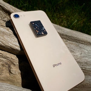 Peut inclure: Un iPhone doré avec une poignée de téléphone mouchetée noire et blanche fixée à l'arrière. Le téléphone porte l'inscription "iPhone" au dos.