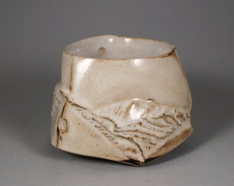 May include: A small, white ceramic bowl with a textured, uneven surface. The bowl has a slightly rounded shape and a wide opening.