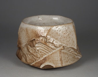 May include: A small, white ceramic bowl with a textured, brown glaze. The bowl has a slightly irregular shape and a wide, rounded rim.