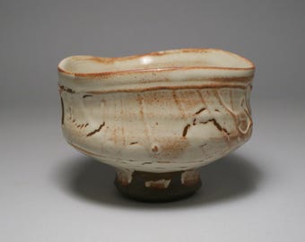 May include: A small, white ceramic bowl with a brown glaze. The bowl has a slightly irregular shape and a small foot.