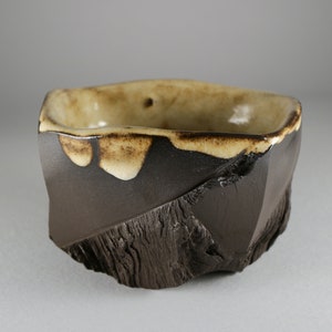 May include: A dark brown ceramic bowl with a light brown glaze on the inside and rim. The bowl has an irregular, textured exterior.