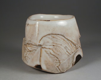 May include: A white ceramic cup with a textured, organic design. The cup has a slightly irregular shape and a wide, open mouth.