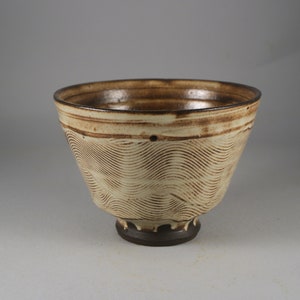 May include: A brown and white ceramic bowl with a wavy pattern. The bowl has a wide rim and a small foot.